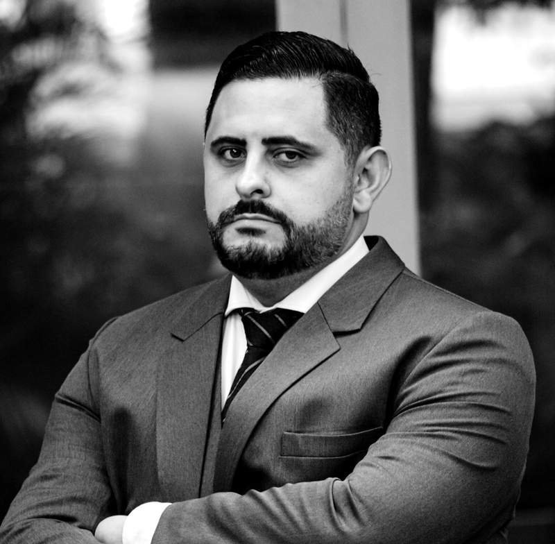 Dr. Isaac Mello, advogado criminalista, de terno e braços cruzados, em retrato em preto e branco